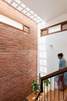 a woman walking up the stairs in a house with red brick walls and wooden handrails