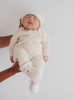 a newborn baby is being held up by someone's hand and wearing a white knitted outfit