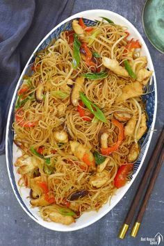 a plate full of noodles and vegetables with chopsticks next to it on a table