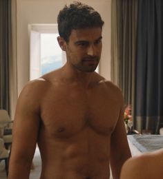 a shirtless man standing in front of a bed