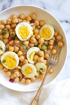 a white bowl filled with eggs and beans next to a fork on top of a table