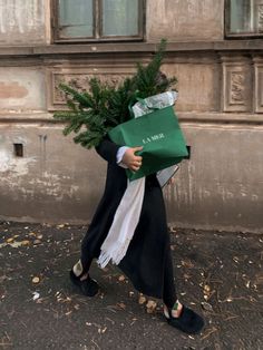 a person walking down the street with a green bag on their head and a christmas tree in his hand