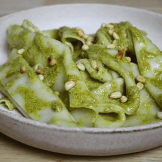 a white bowl filled with green pasta covered in pesto sauce and topped with pine nuts