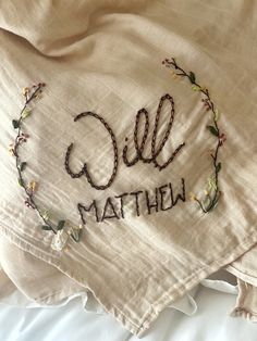 embroidered name on the back of a bed with white linens and floral trim around it