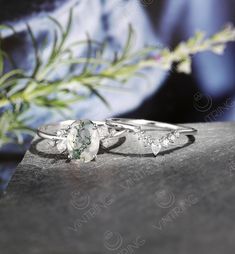 two engagement rings sitting on top of a table next to a flower pot with greenery in the background