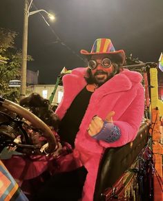 a man in a pink jacket and hat sitting on a motorcycle with his thumbs up