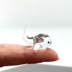 a tiny glass elephant figurine sitting on top of a persons finger in front of a white background