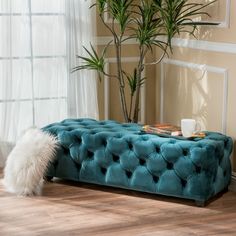 a blue tufted bench in front of a potted plant on a wooden floor