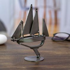 a small metal sailboat on a wooden table next to some reading glasses and eyeglasses