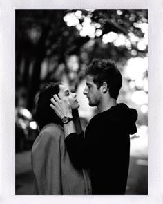 a man and woman standing next to each other in front of a tree with their faces close together