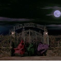 two people sitting on a bench in front of a gate with the moon behind them