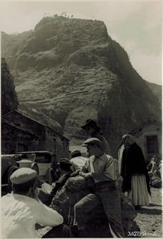 an old black and white photo of people sitting on rocks in front of a mountain