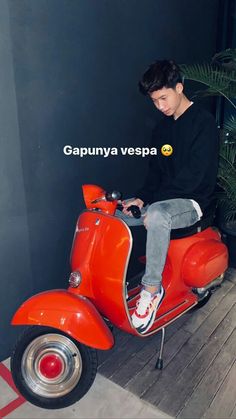 a young man sitting on top of an orange scooter next to a potted plant