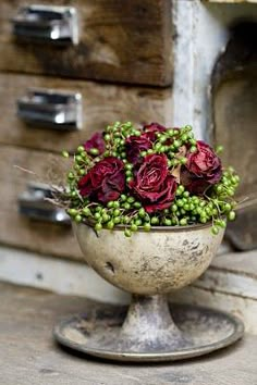 a vase filled with red flowers sitting on top of a wooden table next to drawers