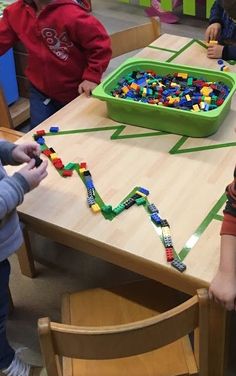 two children playing with legos at a table in a playroom while another child watches