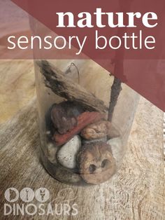 a glass jar filled with rocks on top of a wooden table next to a sign that says nature sensory bottle