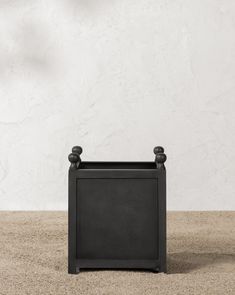 a small black planter sitting on top of a carpeted floor next to a white wall