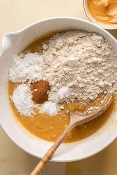 a white bowl filled with dry ingredients next to a wooden spoon on top of a table