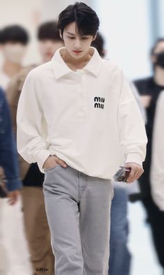 a young man walking down a runway with his hands in his pockets and wearing grey pants