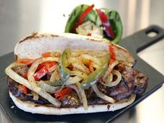 a close up of a sandwich on a plate with peppers and onions in the background