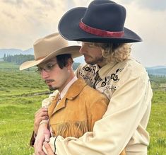 two men in cowboy hats standing next to each other on a green grass covered field