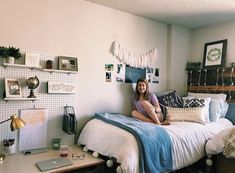 a woman sitting on top of a bed next to a desk and laptop computer in a bedroom