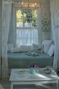 a bed sitting under a window next to a table with plates and cups on it