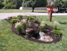 there is a small garden with rocks and flowers in the grass next to a street sign