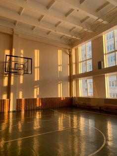 an empty basketball court with sun shining through the windows