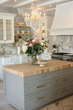 a kitchen island with flowers on it in front of a chandelier and cabinets