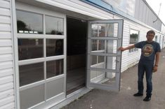 a man is holding up an open door to the side of a building that has windows