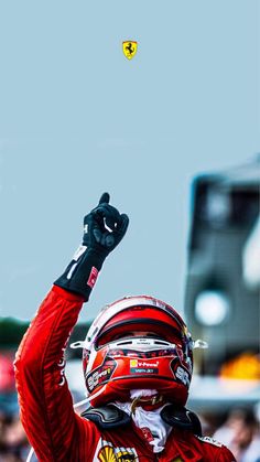 a man in a racing suit holding his fist up to the sky while wearing a helmet