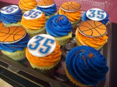 cupcakes decorated with blue and orange frosting are displayed in a display case