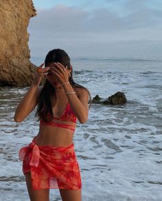 a woman standing on the beach with her hands to her face