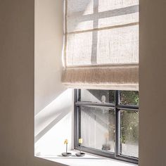 an open window in a white room with two candles on the windowsill and one light coming through