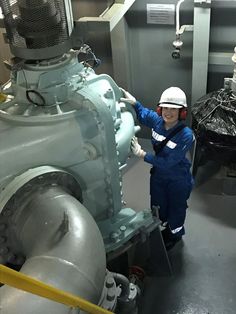 a man in blue coveralls and safety gear standing next to a large machine