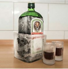 a bottle and two glasses sitting on a table next to each other with ice cubes around it