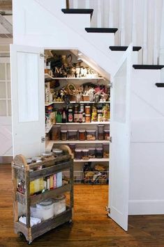 an open pantry under a stair case in a room with wooden floors and white walls