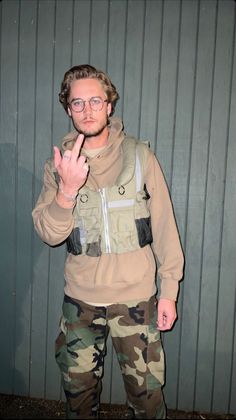 a man in camo is making the peace sign with his hand while standing against a wall