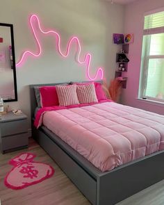 a bed with pink comforter and pillows in a room that looks like it has neon lights on the headboard