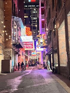 an alley way with neon signs and people walking down it