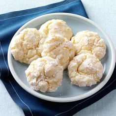 a white plate topped with snowball cookies on top of a blue cloth next to a knife and fork