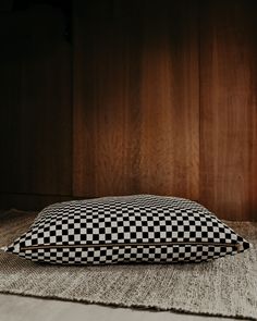 a black and white checkered pillow sitting on top of a bed next to a wooden wall