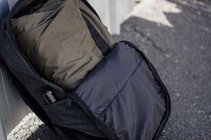 an empty black backpack sitting on the side of a road next to a pole and fence