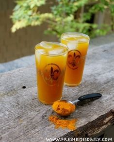 two glasses filled with liquid sitting on top of a wooden table next to a spoon