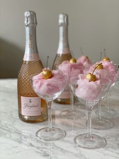 three wine glasses filled with ice cream and topped with cherries next to two bottles of champagne