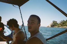 two men sitting on a boat in the water while another man stands next to them