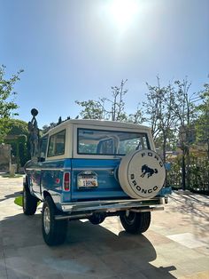 a blue truck parked on top of a stone walkway next to trees and bushes with a statue in the background