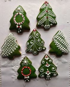 six decorated christmas trees are arranged on a white doily with red and green beads