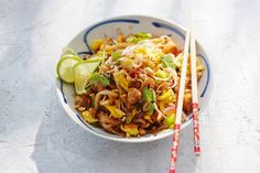 a bowl filled with noodles and vegetables next to two chopsticks on a table